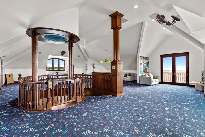 Spacious room with sloped ceilings, a prominent wood-finish stairwell, and a double-door balcony access