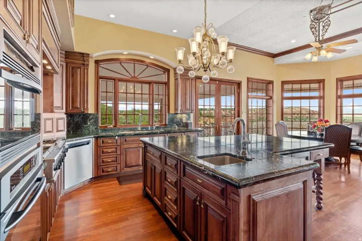Custom cabinetry, built-in stainless steel appliances, central island with integrated sink, stone countertops, and wood-finish flooring