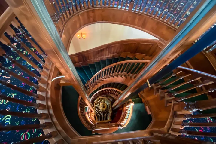 Multi-level spiral staircase featuring wood-finish railings, ornate balusters, and a decorative ceiling fixture
