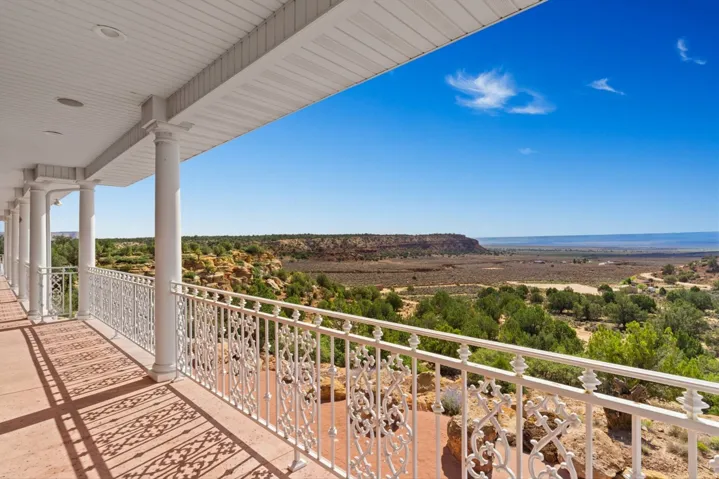 Covered balcony with white columns, decorative white railing, and expansive distant landscape