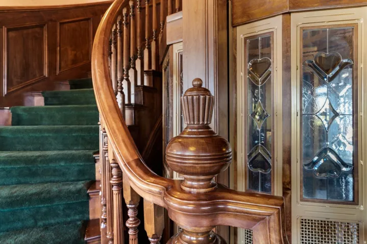 Hardwood staircase with ornate newel post and balusters, green carpeted treads, and wood paneling