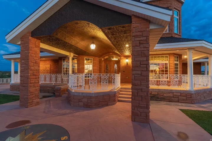 Stone-clad exterior featuring multiple windows, a covered entry with an ornate ceiling, and a concrete pathway with an inlaid compass design