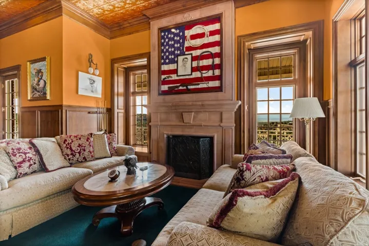 Detailed wood paneling, textured ceiling, stone-clad fireplace, and multiple windows with wood trim