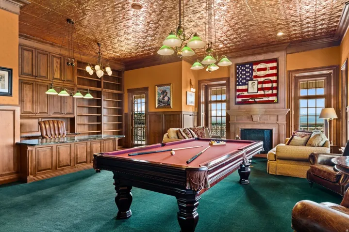 Recessed fireplace with stone surround, wood-paneled walls, built-in wooden cabinetry, custom built-in shelving, and a decorative ceiling