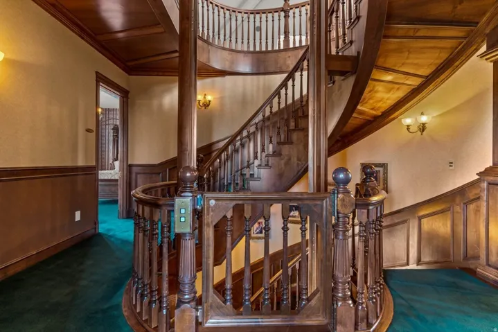Curved wood staircase with intricate baluster detailing, wood paneling, and wood-finish ceiling accents