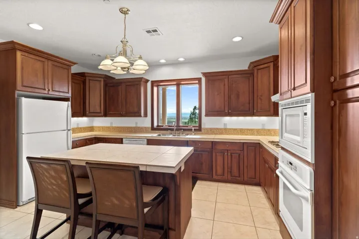 Kitchen featuring wood cabinetry, a center island with bar seating, tile flooring, and integrated white appliances
