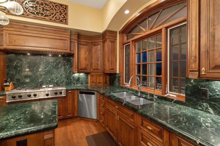 Arched window with wood trim, stainless steel appliances, dual basin sink, wood-finish flooring, and green stone countertops