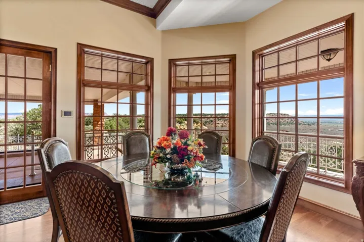 Wood-finish flooring with a circular dining table, surrounded by multiple windows with grid patterns, and a glass door leading to a patio