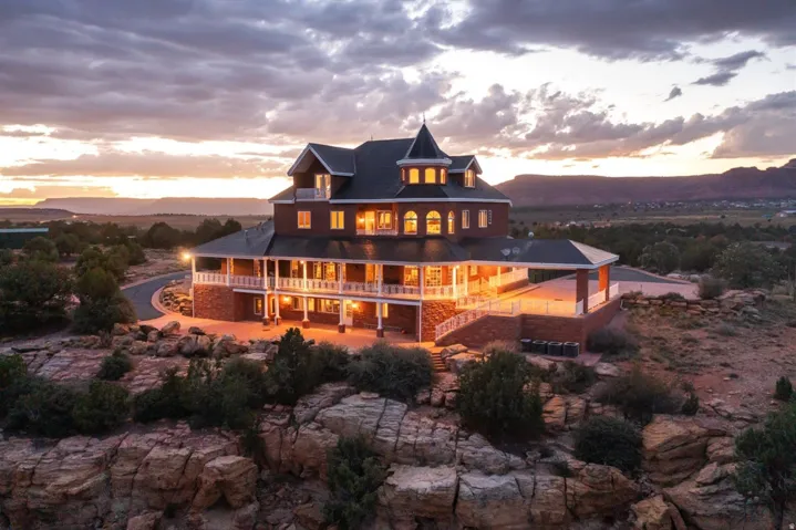 Multi-level property featuring a turret, extensive wrap-around balcony, brick exterior, and prominent red rock landscape