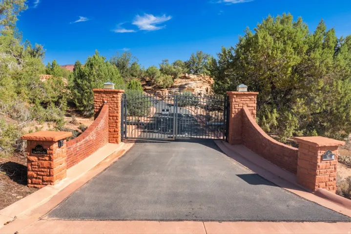 Gated entrance featuring stone pillars, wrought iron gates, and an asphalt driveway