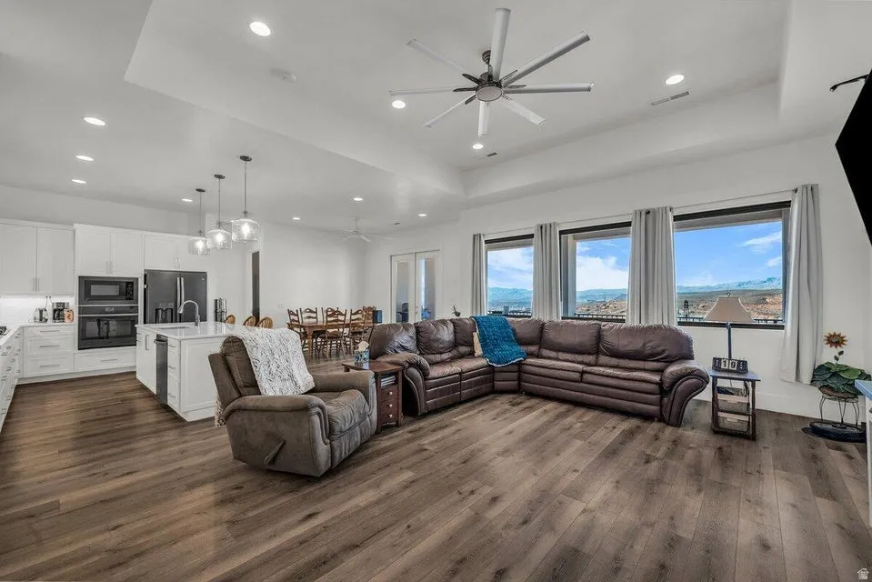 Living room featuring a ceiling fan, a tray ceiling, dark wood-style floors, healthy amount of natural light, and recessed lighting