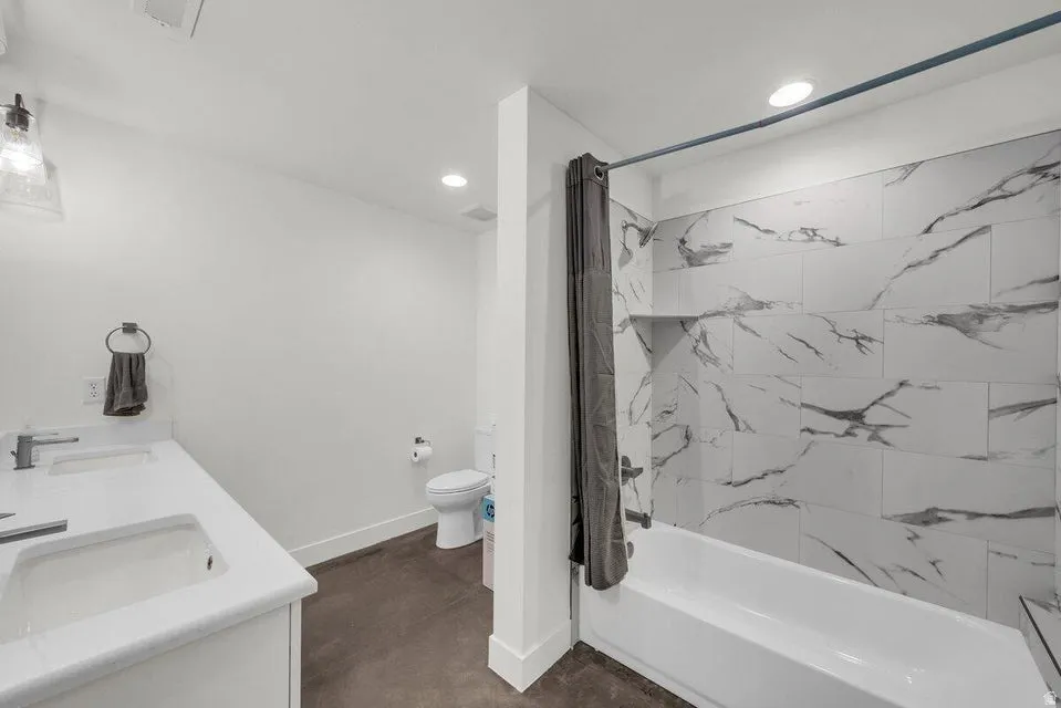 Full bath with double vanity, shower / tub combo, recessed lighting, and finished concrete floors