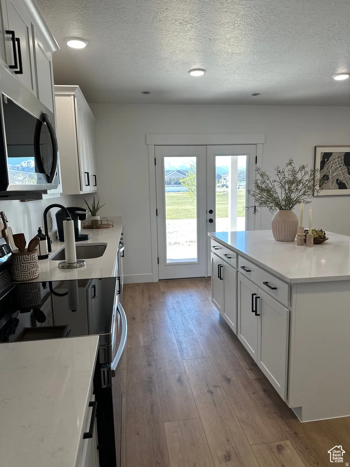 Kitchen with white cabinetry, light stone countertops, stainless steel microwave, a textured ceiling, and black range with electric stovetop