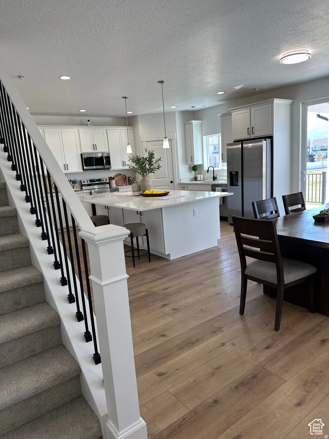 Kitchen with stainless steel appliances, light wood finished floors, a breakfast bar area, white cabinetry, and a textured ceiling