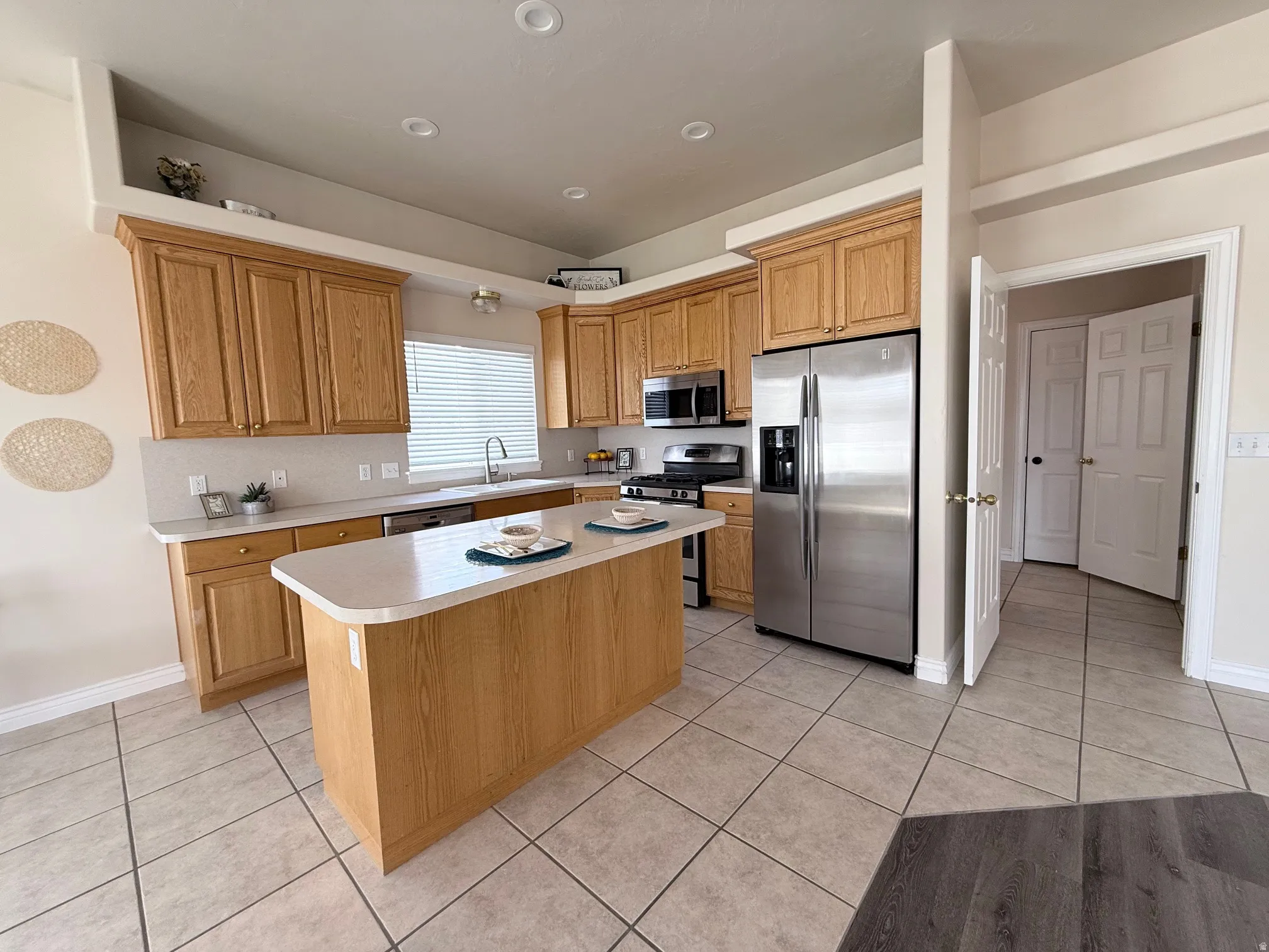 Kitchen featuring stainless steel appliances, light countertops, light tile patterned floors, a kitchen island, and wood finish cabinets