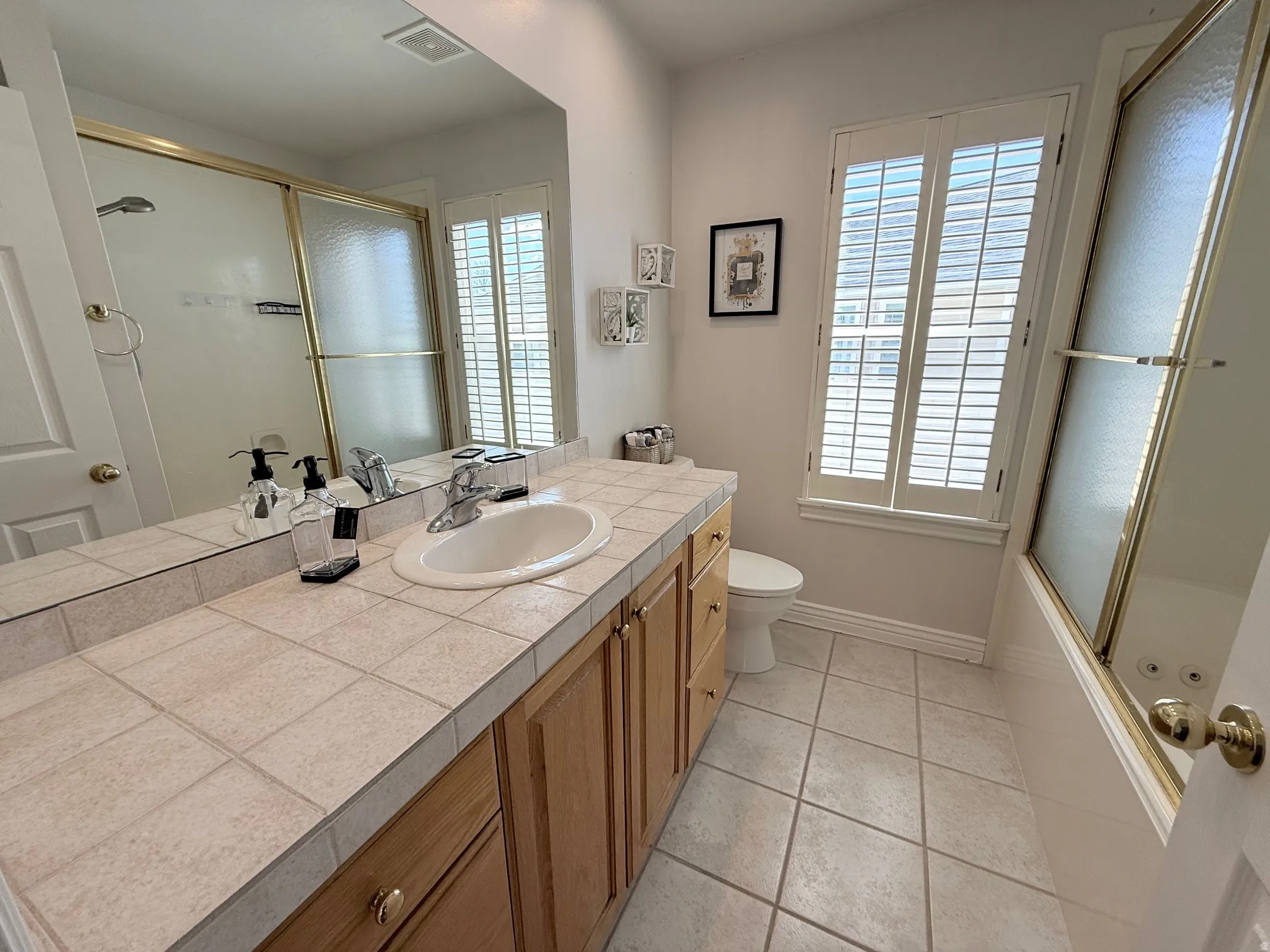 Bathroom with enclosed tub / shower combo, light tile patterned floors, and vanity