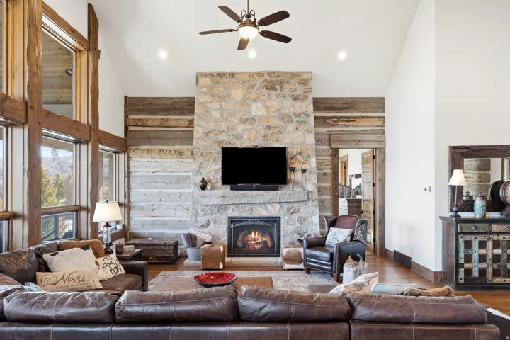 Living room with hardwood / wood-style floors, a ceiling fan, a stone fireplace, vaulted ceiling, and wooden walls