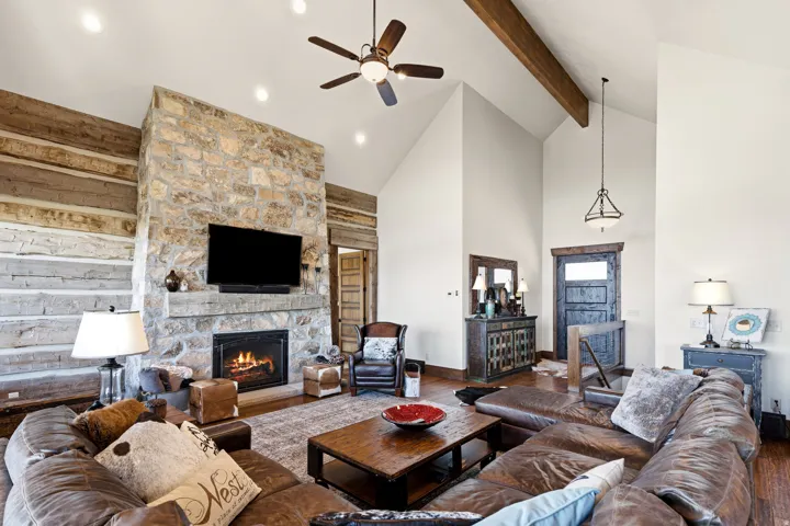Living area featuring wood finished floors, a stone fireplace, and a ceiling fan