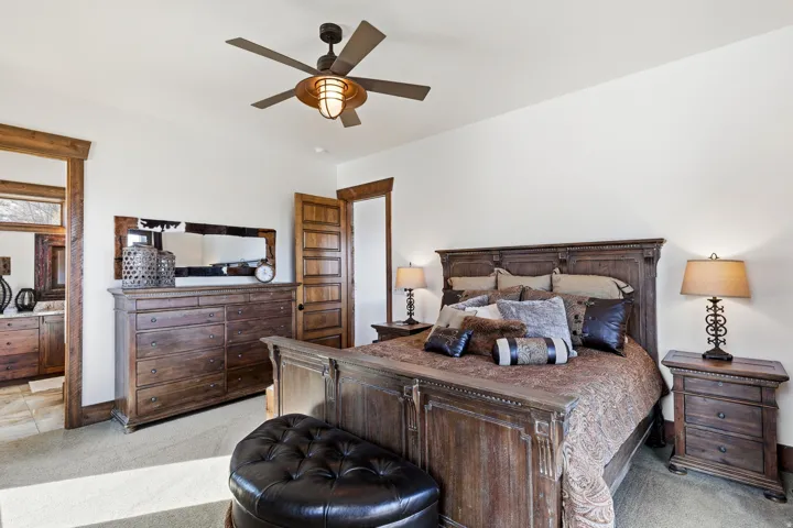 Bedroom with ceiling fan, light colored carpet, and ensuite bath