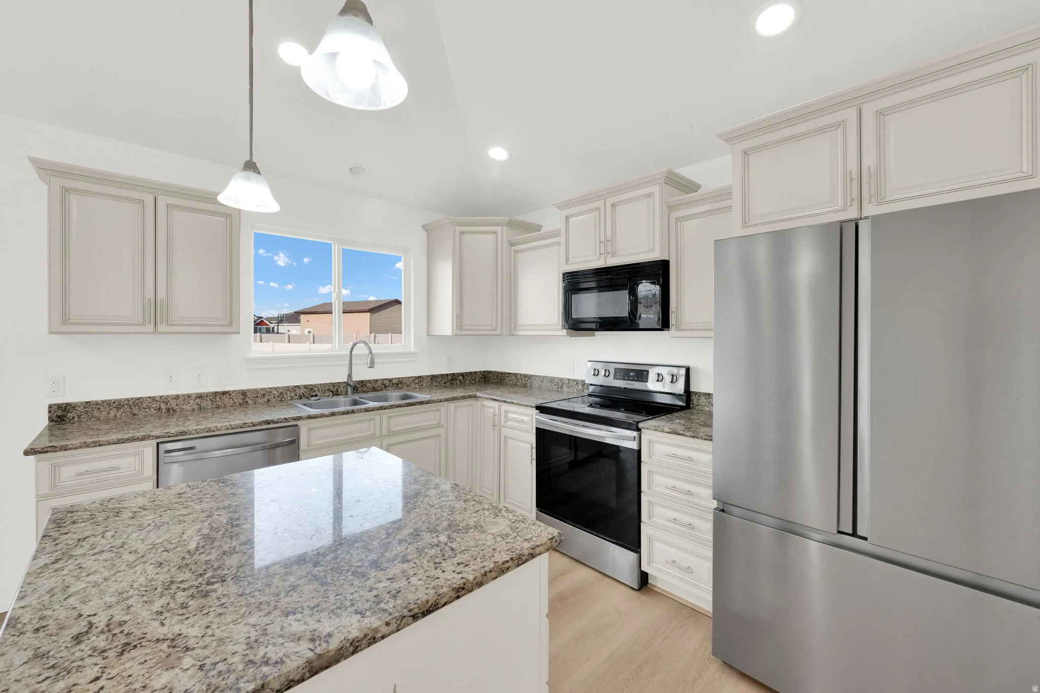 Kitchen featuring stainless steel appliances, light stone countertops, pendant lighting, light wood-style flooring, and cream cabinetry