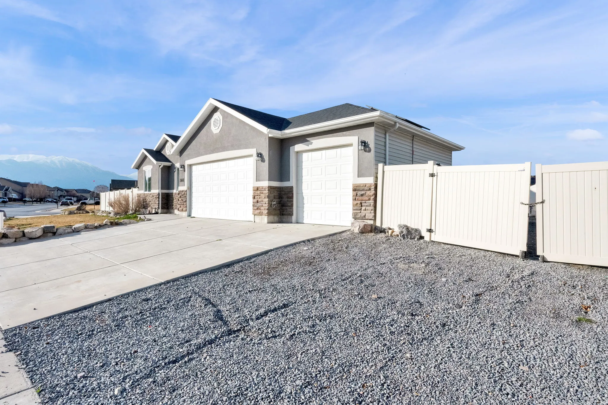 View of side of property featuring a gate, an attached garage, concrete driveway, stone siding, and stucco siding