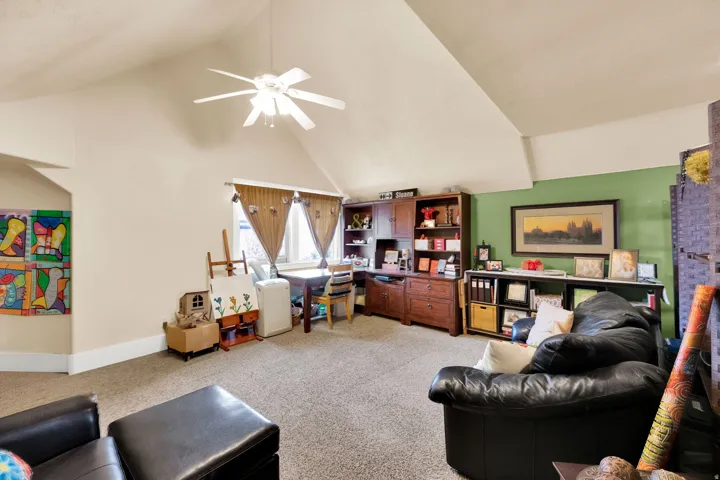 Living room featuring light colored carpet, a ceiling fan, a high ceiling, and a desk