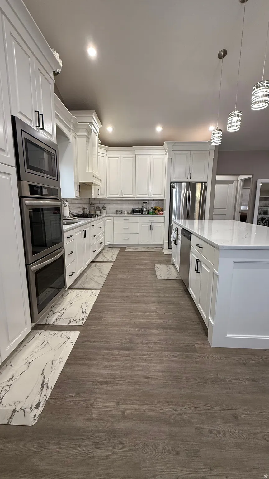 Kitchen featuring white cabinetry, decorative backsplash, stainless steel appliances, and decorative light fixtures