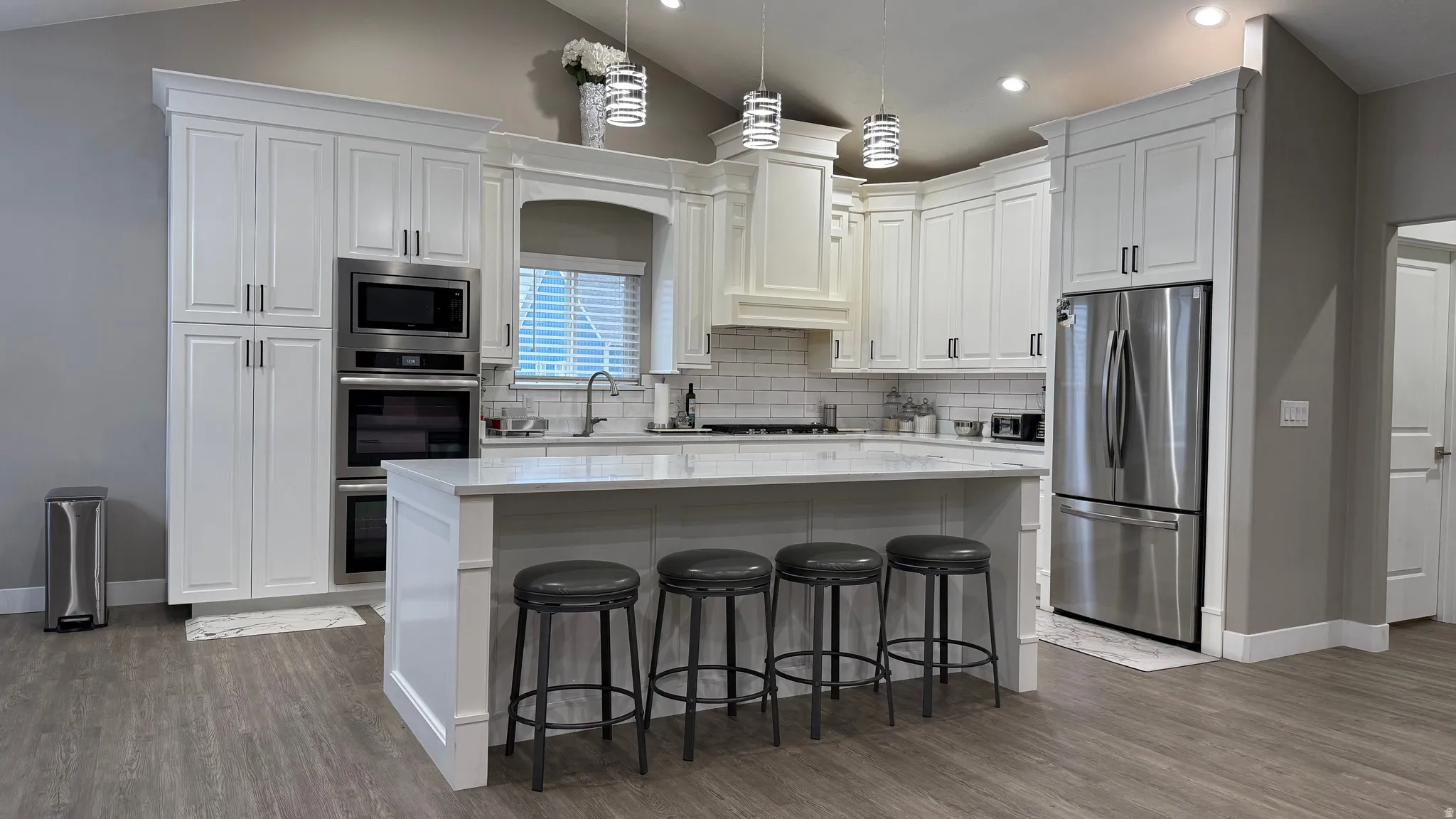 Kitchen with stainless steel appliances, white cabinetry, a breakfast bar, lofted ceiling, and dark wood finished floors
