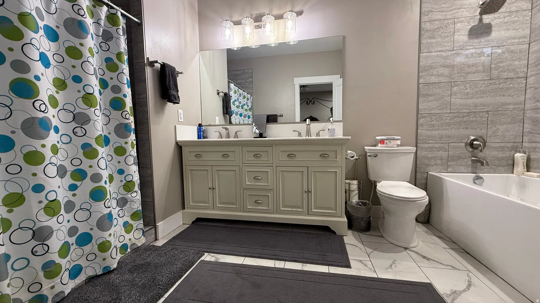 Full bathroom featuring double vanity, light marble finish flooring, and shower / bath combination with curtain