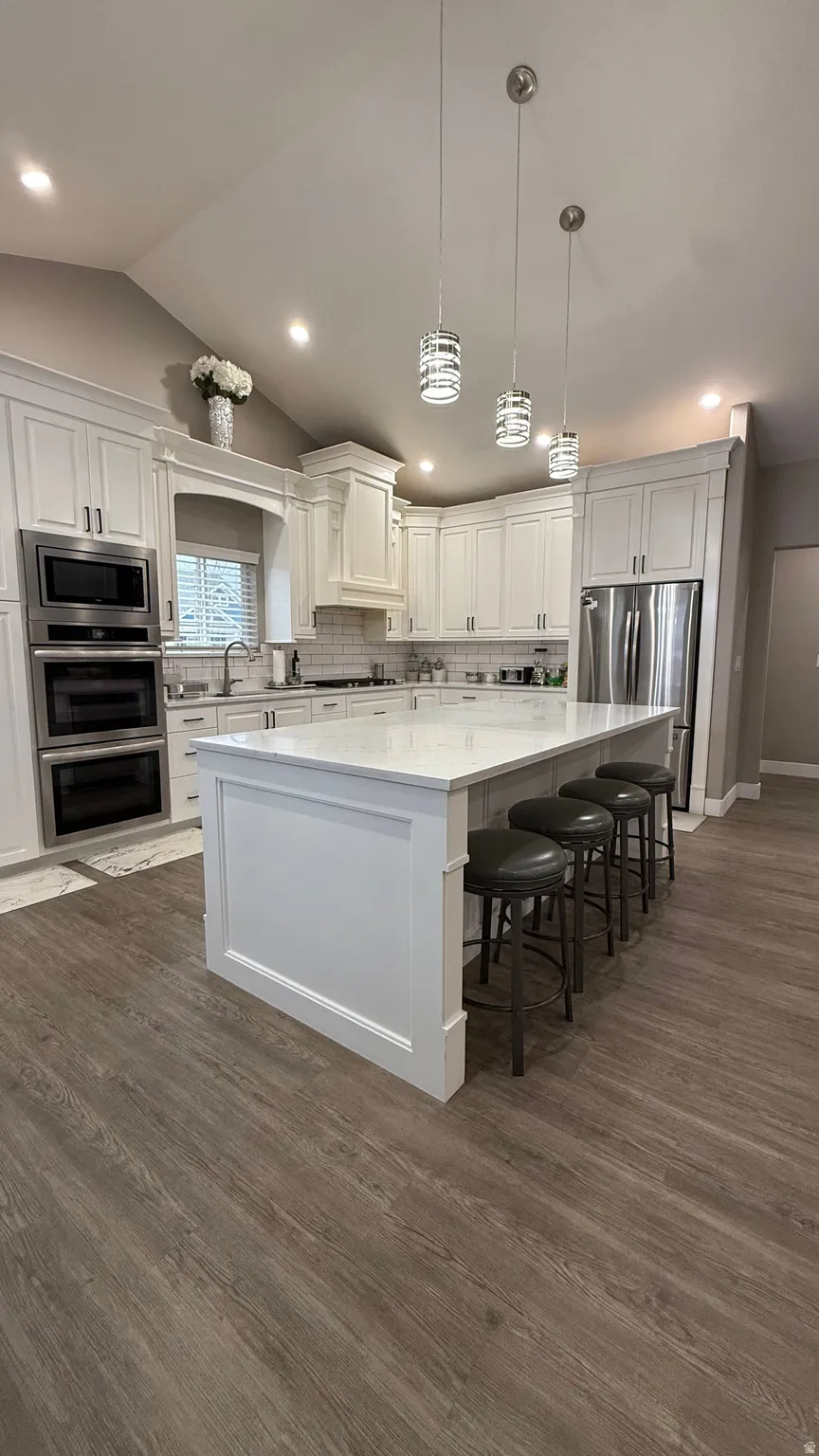 Kitchen with white cabinets, a large island, stainless steel appliances, decorative backsplash, and dark wood-style flooring