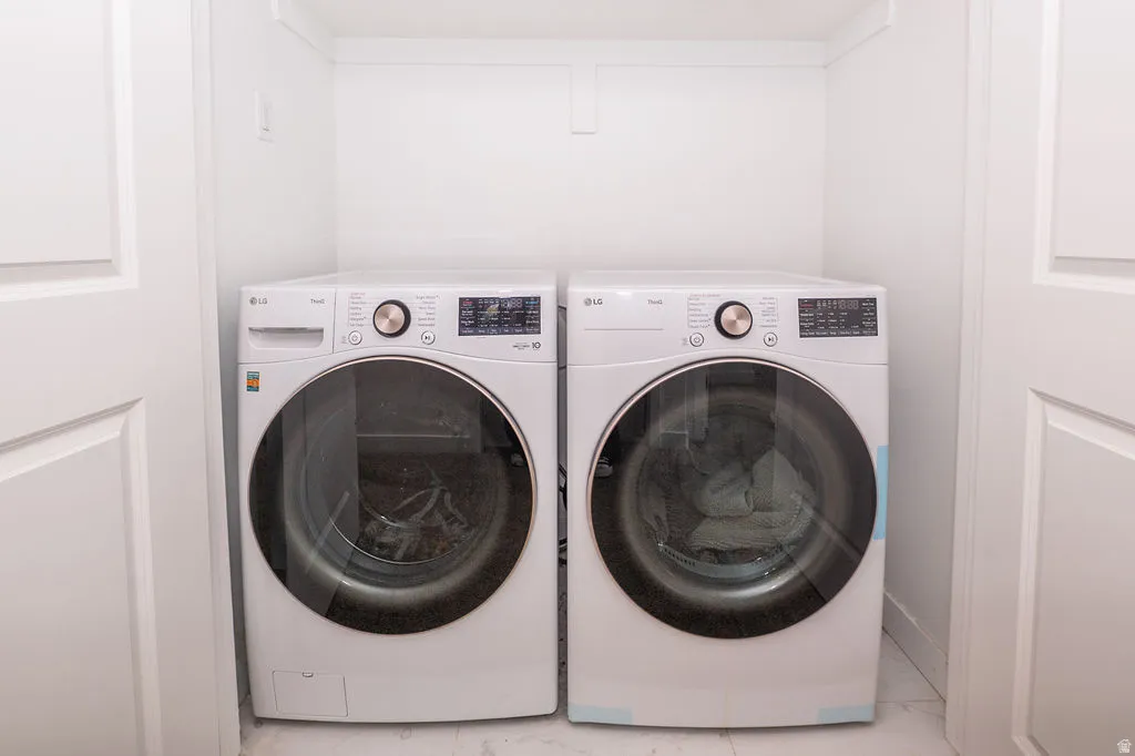 Laundry area with washer and clothes dryer and light marble finish flooring