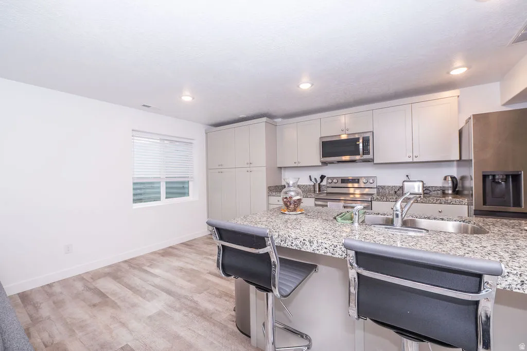 Kitchen featuring stainless steel appliances, a breakfast bar, light wood finished floors, light stone counters, and recessed lighting