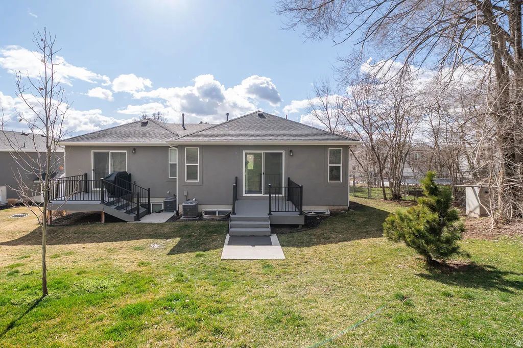 Back of house with a shingled roof, stucco siding, and a lawn