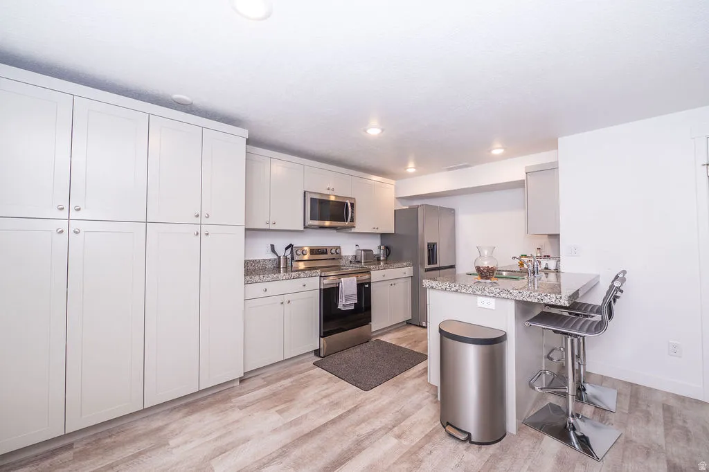Kitchen with stainless steel appliances, a peninsula, a kitchen breakfast bar, light wood-style floors, and light stone countertops