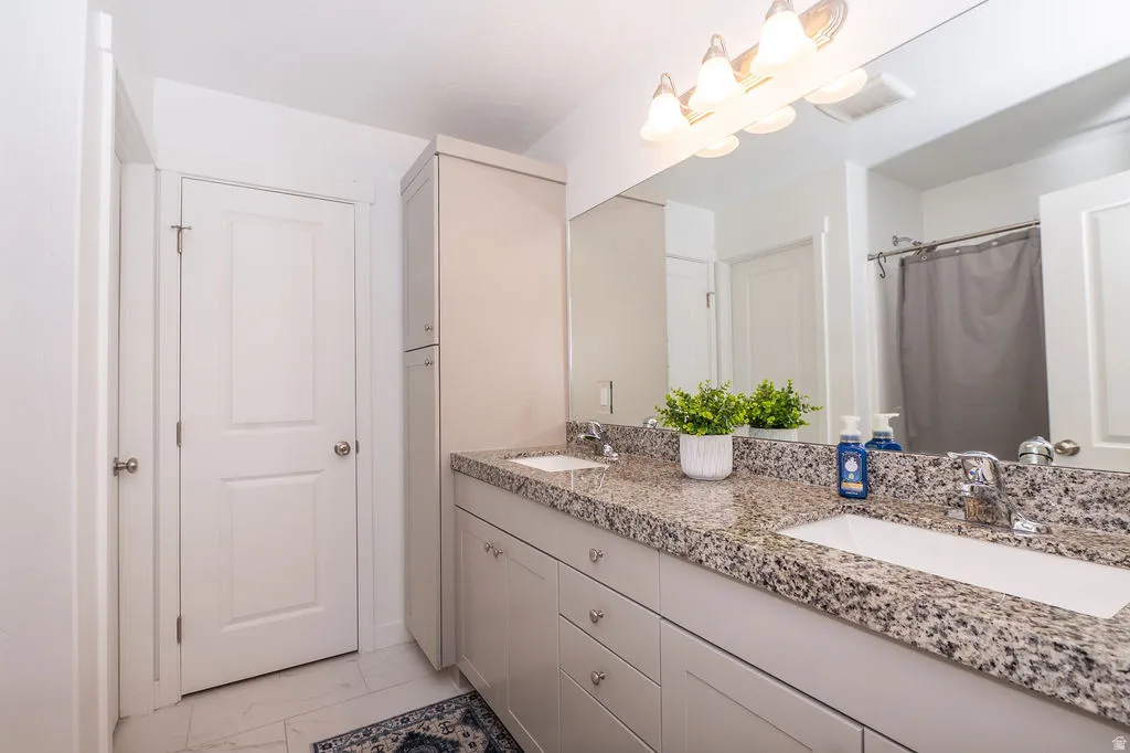 Bathroom featuring double vanity, a shower with curtain, and light marble finish floors