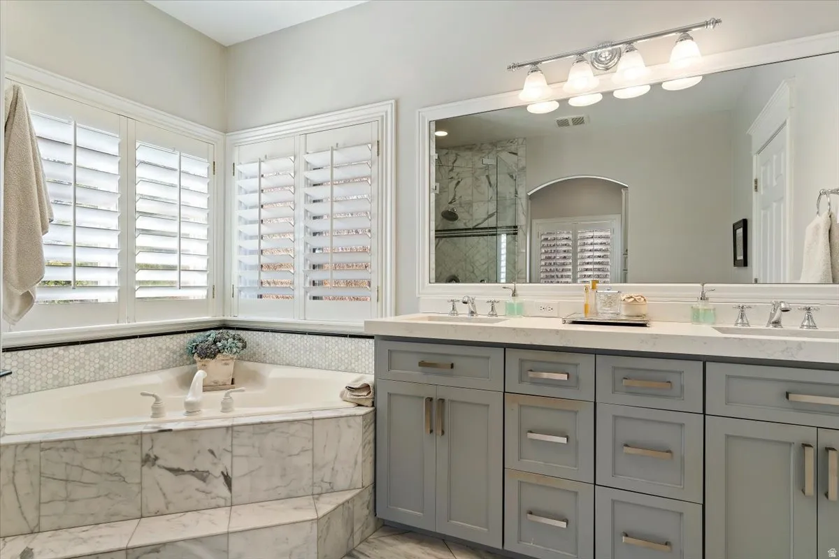 Bathroom with double vanity, a marble finish shower, and a bath