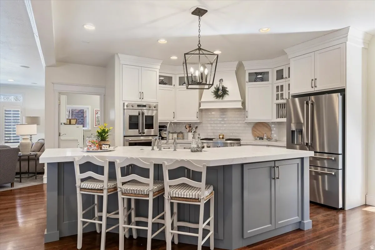 Kitchen with stainless steel appliances, glass fronted cabinets, dark wood-style flooring, a breakfast bar area, and two tone color scheme
