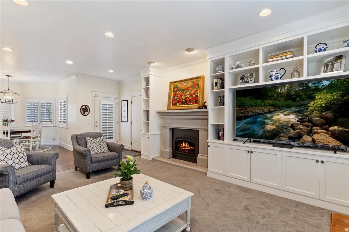 Living room featuring ornamental molding, a warm lit fireplace, built in shelves, and recessed lighting
