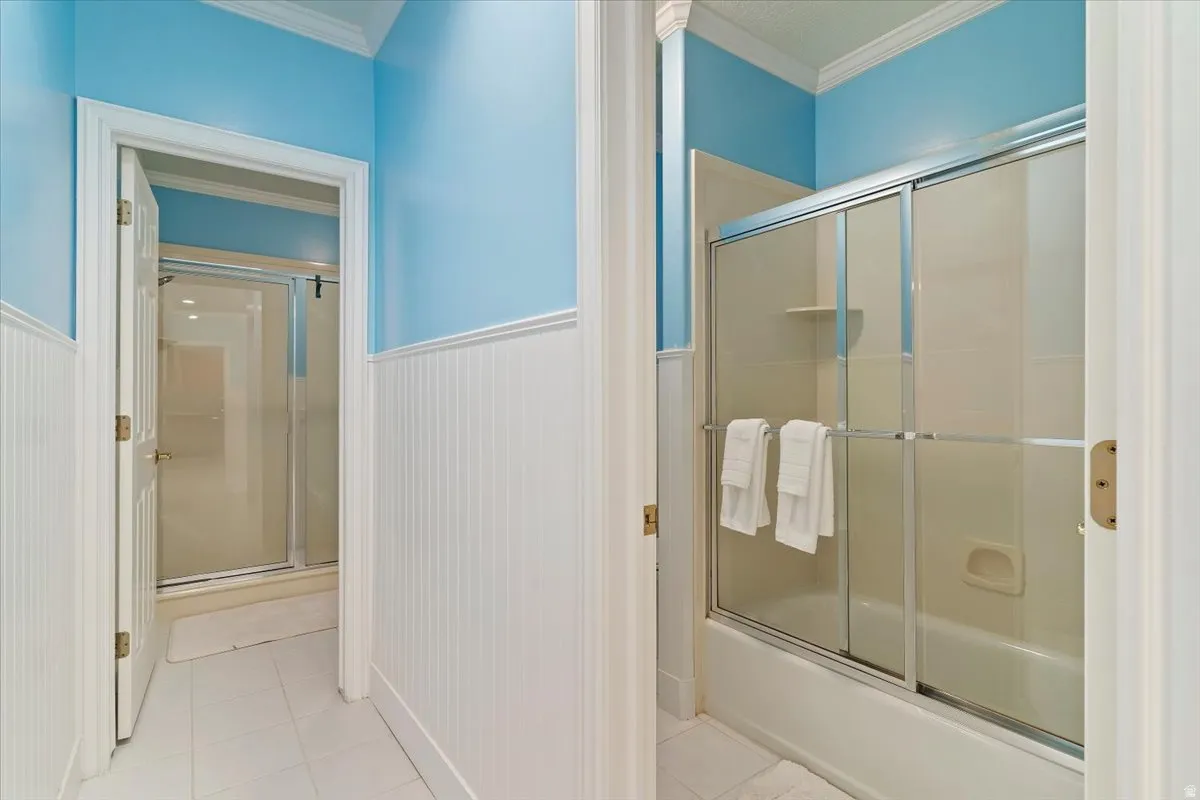 Full bath featuring wainscoting, crown molding, enclosed tub / shower combo, and light tile patterned floors