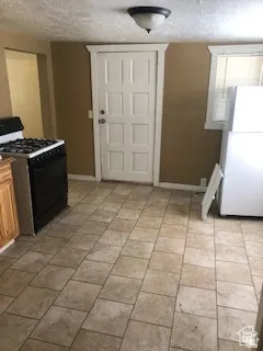 Kitchen featuring black range with gas cooktop, freestanding refrigerator, and a textured ceiling