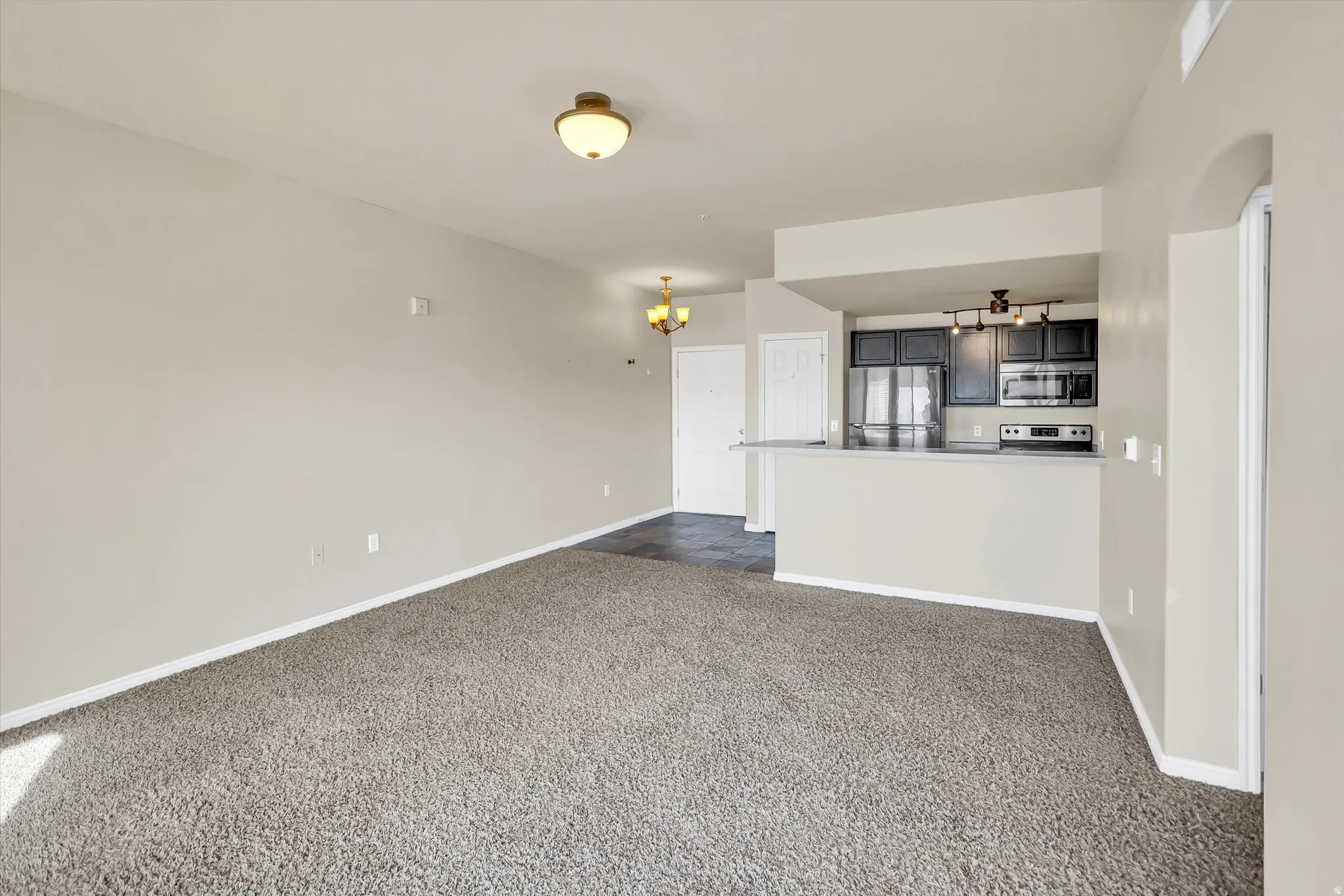 Unfurnished living room featuring hanging lights, dark colored carpet, and arched walkways