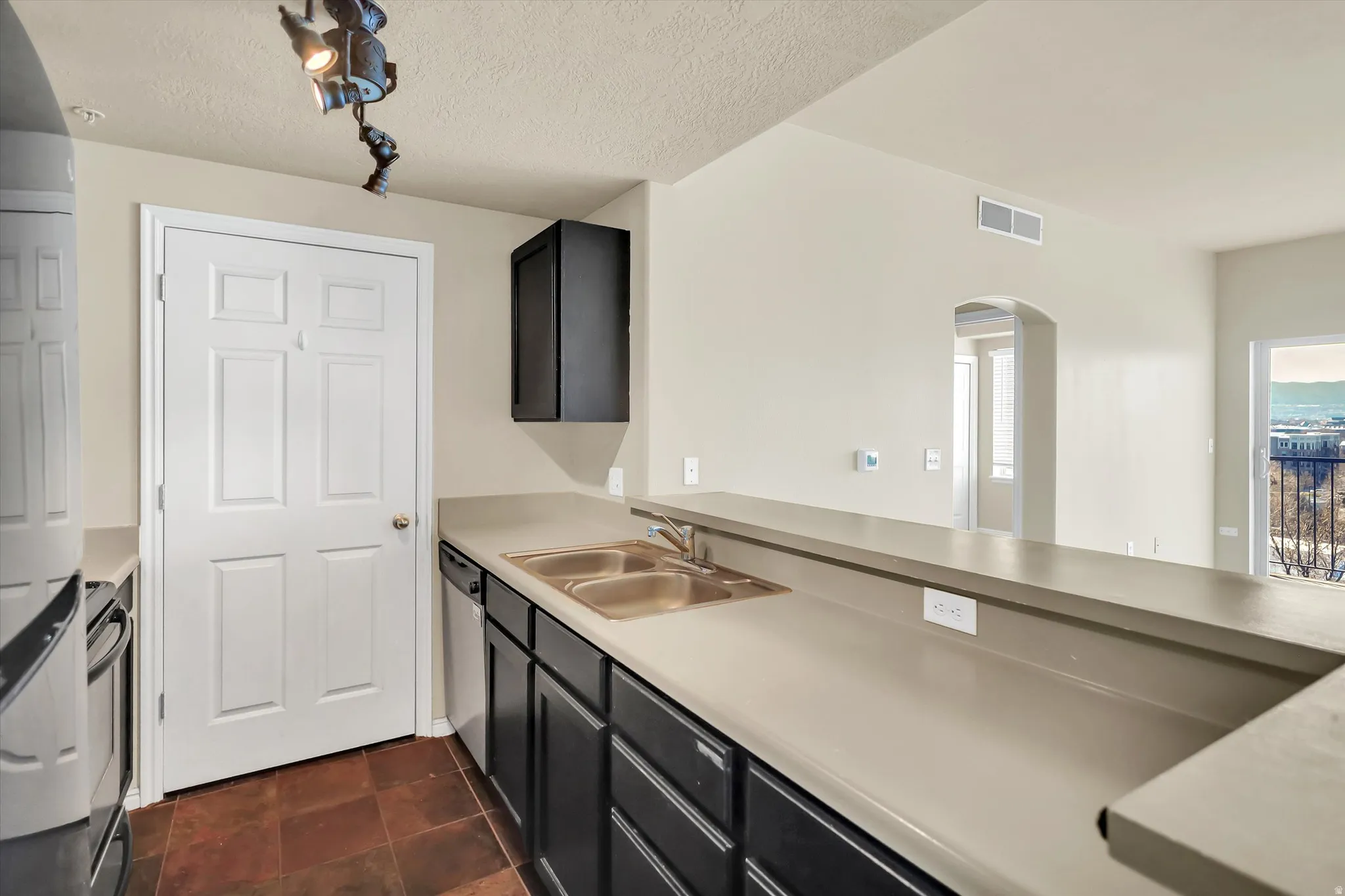 Kitchen with dark cabinetry, arched walkways, a textured ceiling, light countertops, and fridge