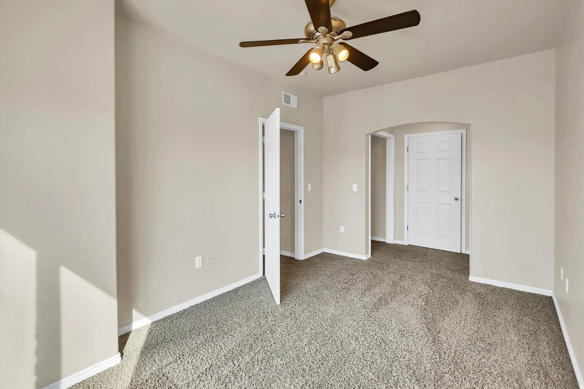 Unfurnished bedroom featuring light carpet, arched walkways, and a ceiling fan