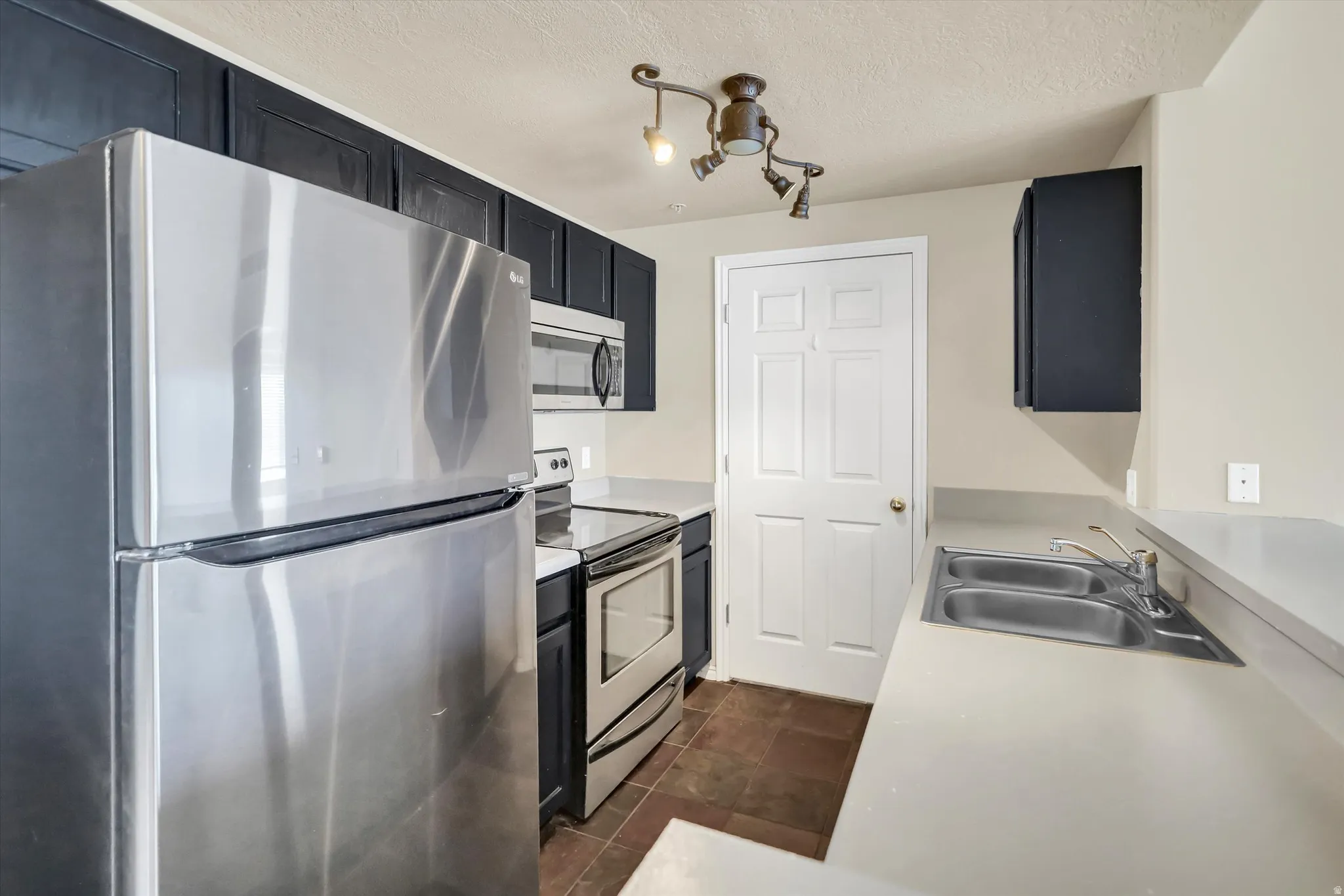 Kitchen featuring stainless steel appliances, dark cabinetry, light countertops, a textured ceiling, and dark tile patterned flooring
