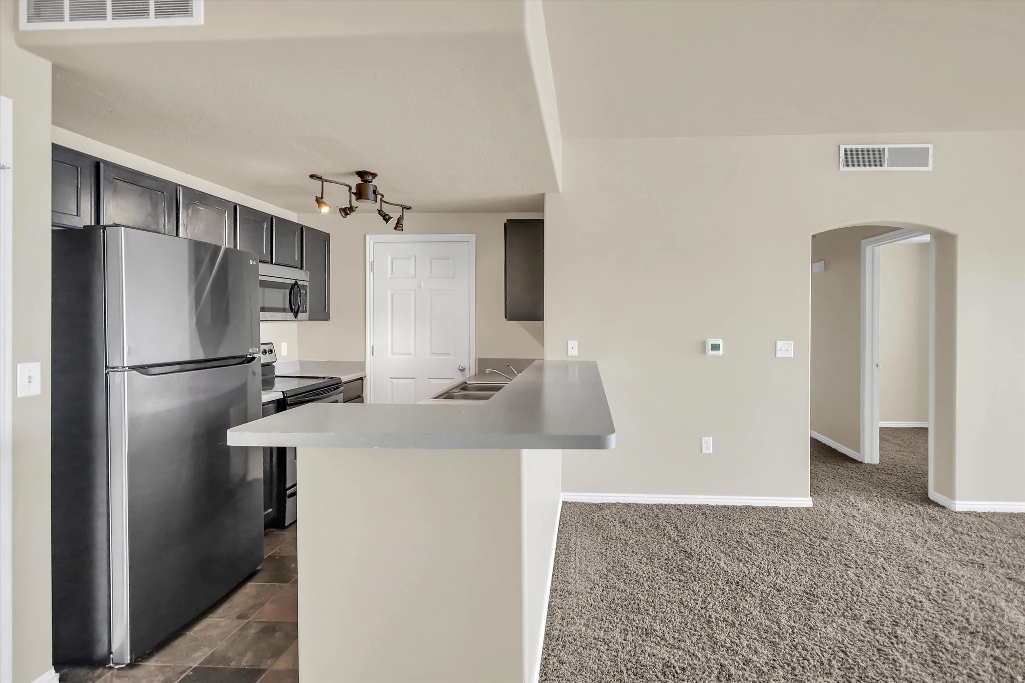 Kitchen with stainless steel appliances, arched walkways, light countertops, a peninsula, and dark carpet