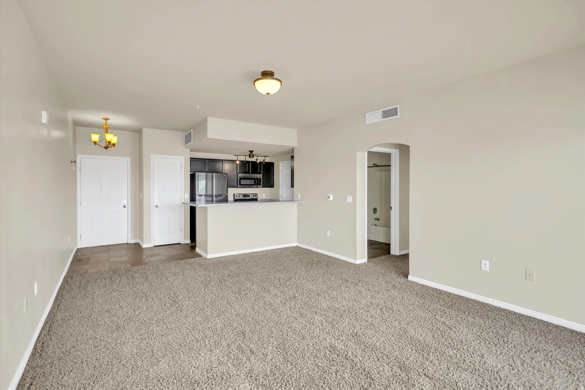 Unfurnished living room with arched walkways, dark colored carpet, and hanging lights