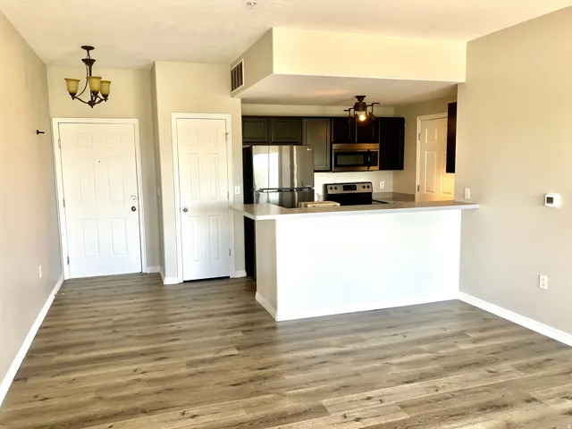 Open concept living space featuring wood-finish flooring, a kitchen with dark cabinetry and stainless steel appliances, a breakfast bar, and neutral wall tones