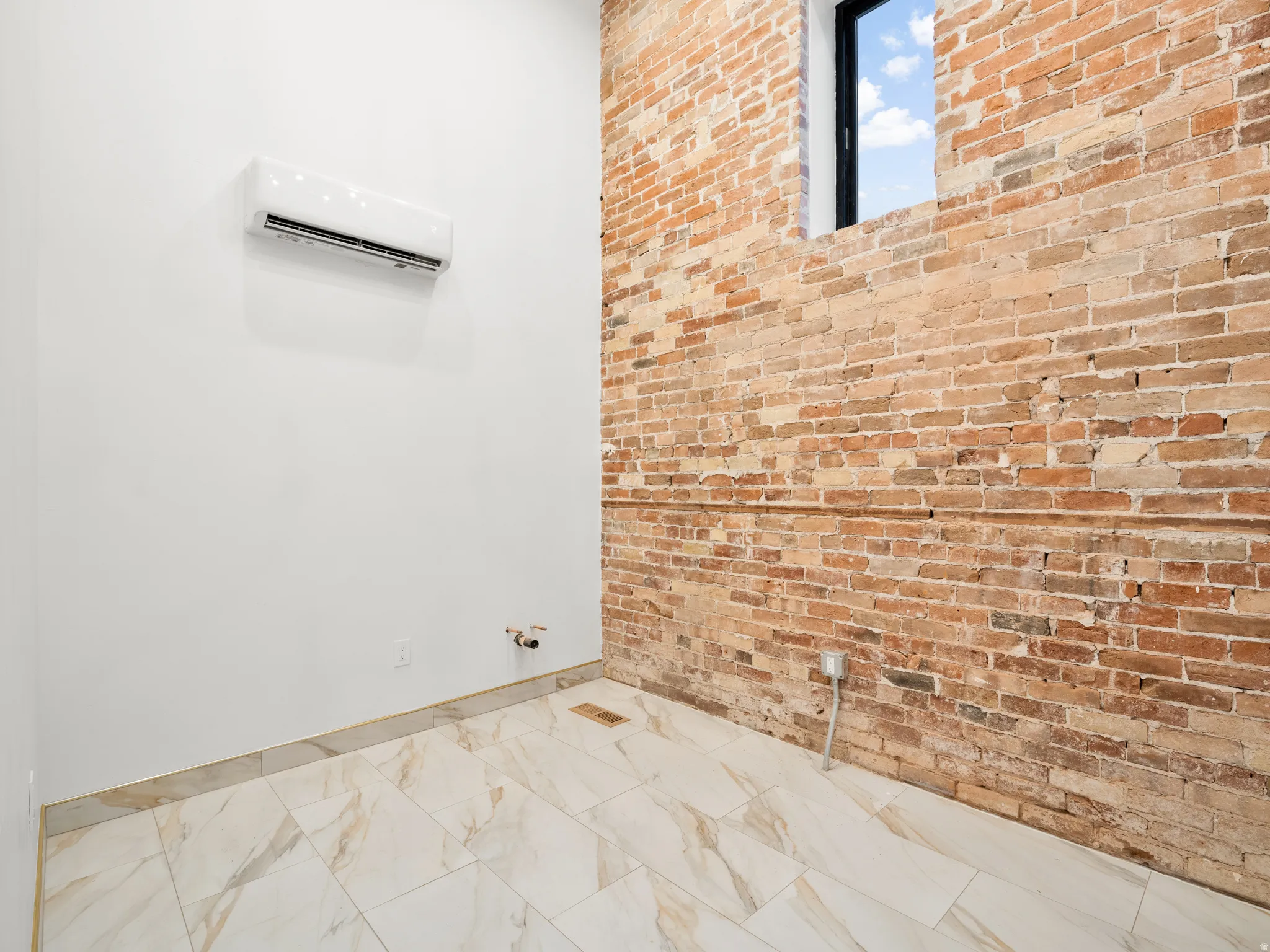 Bathroom featuring brick wall, a mini split for heating / cooling, and light marble finish flooring
