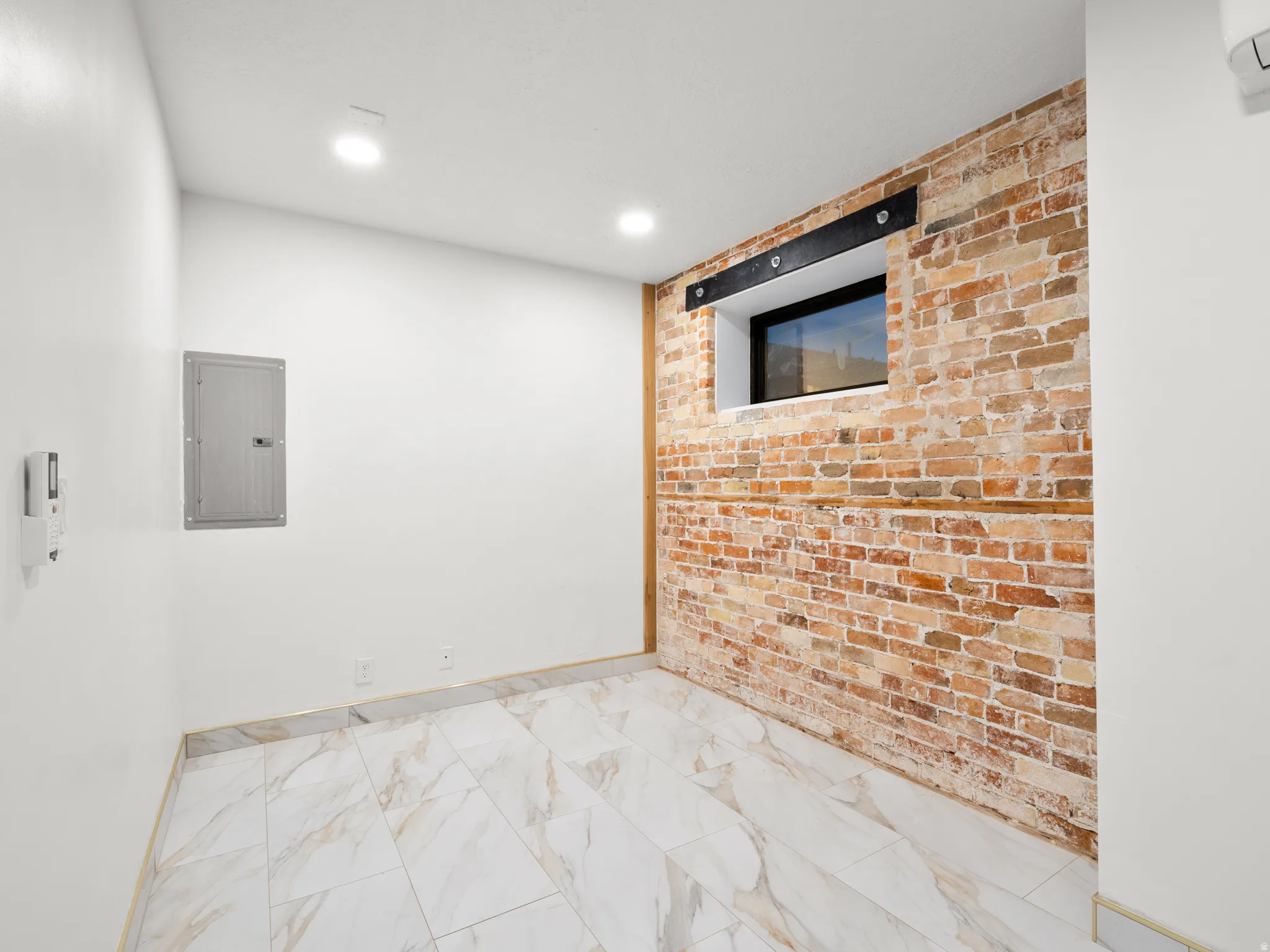 Spare room with brick wall, electric panel, recessed lighting, and light marble finish floors