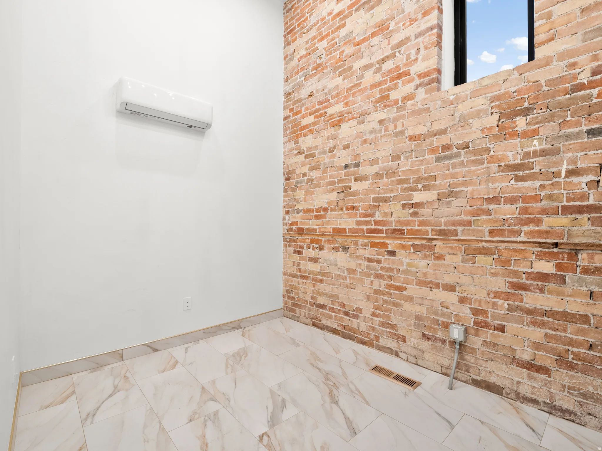 Bathroom with brick wall, a wall mounted mini split, and light marble finish flooring